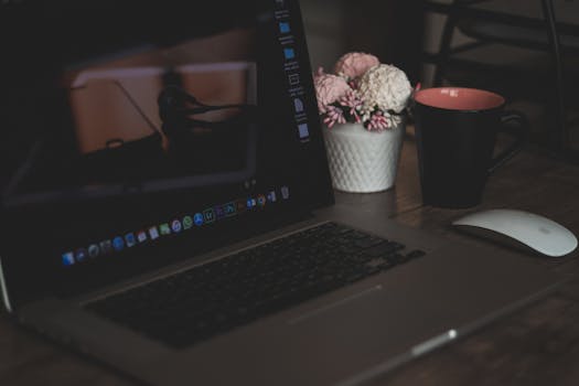 A cozy workspace featuring a laptop, coffee cup, and artificial flowers, ideal for remote work.