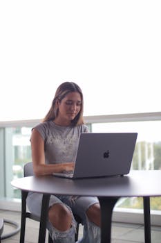 Young woman using laptop at indoor study space with natural light.